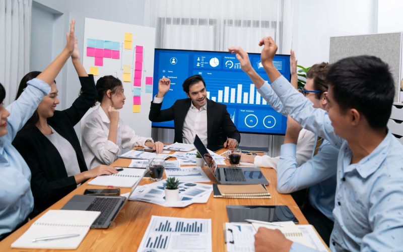 Group of happy multi ethnic businesspeople in celebratory gesture and successful teamwork after made success sales or positive financial data dashboard display on screen in meeting room. Habiliment